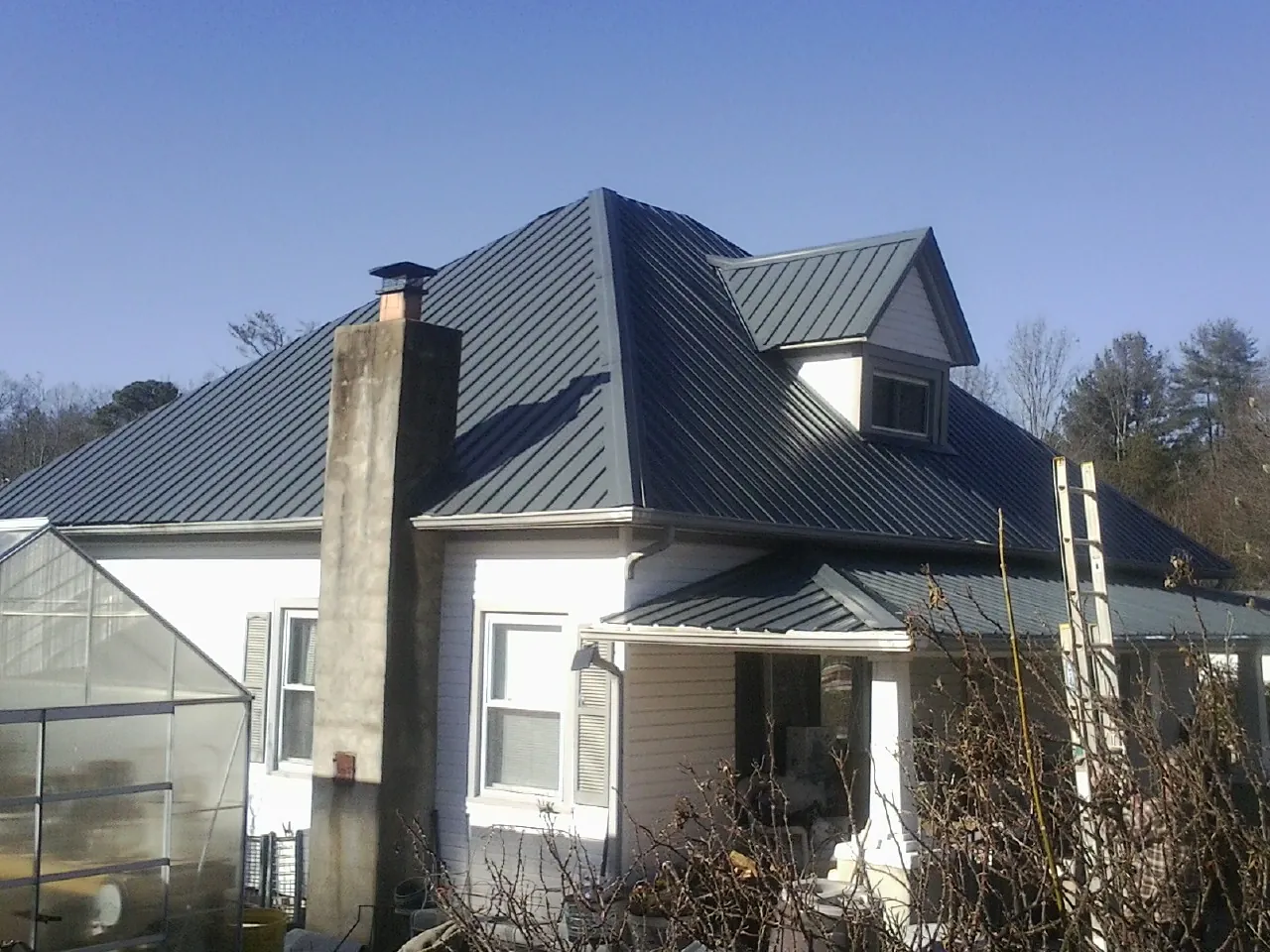 Dark blue standing seam metal roof on a white farmhouse with dormer — Slate & Tile Roof Repair by Roofing Brothers in Bernard