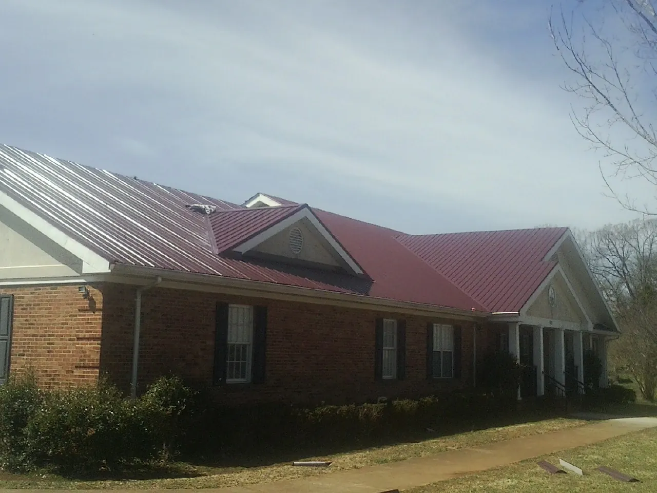 Red metal roof with gabled entries on a long brick building, from a Hail Damage Roof Repair job in Bernard
