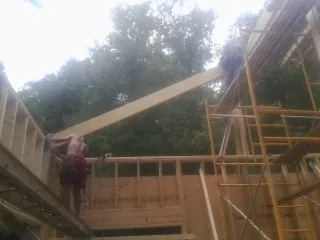 Carpenter raising a rafter beam on a new second story frame in Bernard