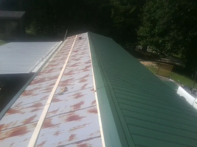 Old rusted panels beside newly installed green metal roofing — Wind Damage Roof Repair by Roofing Brothers in Bernard