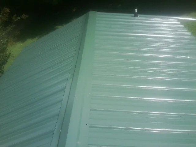 New green metal panels meeting at the ridge of a roof — Flat Roof Repair work by our crew in Bernard