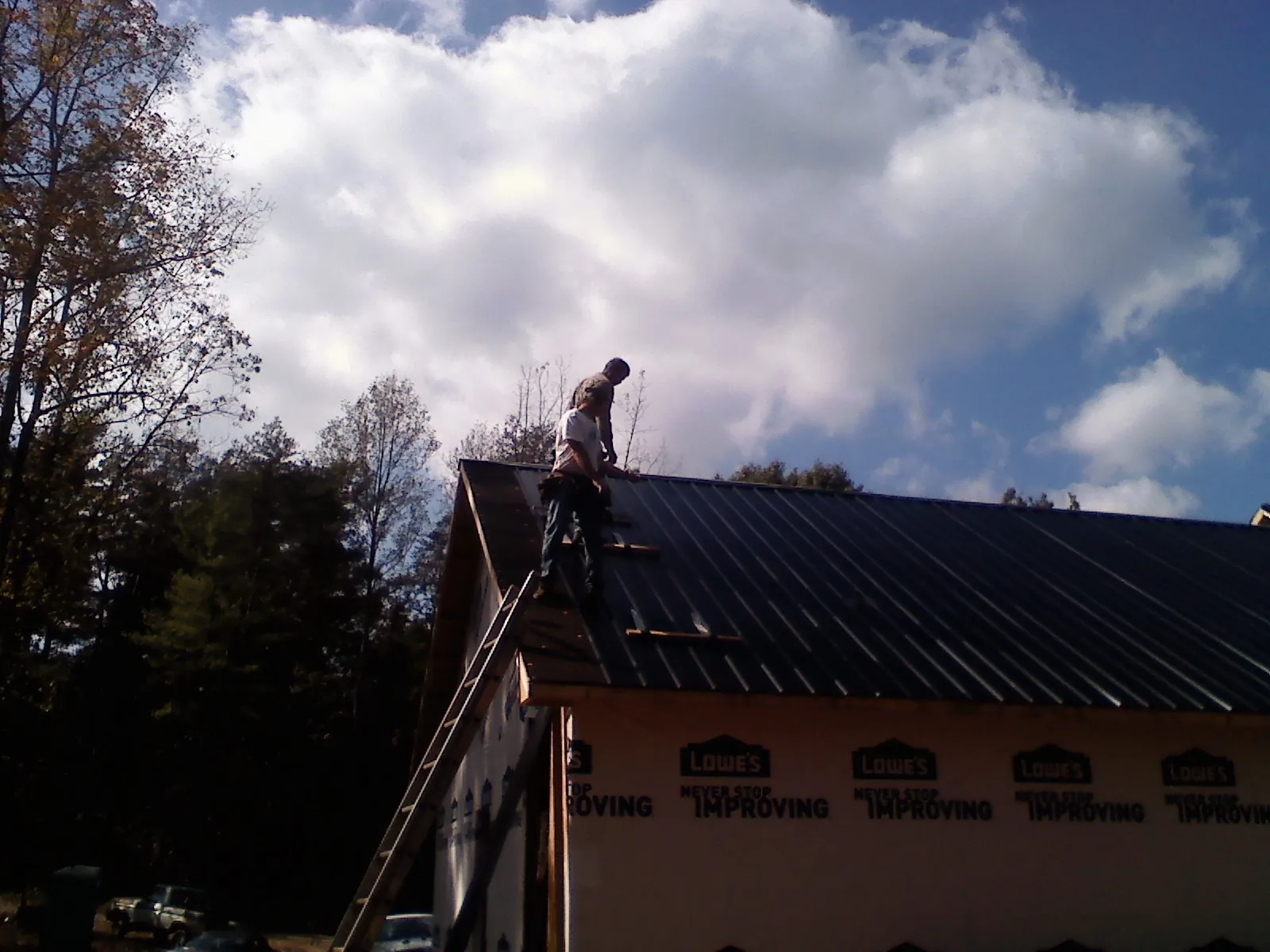 Roofer fastening dark metal panels high against a cloudy sky, from a Roof Inspection job in Bernard