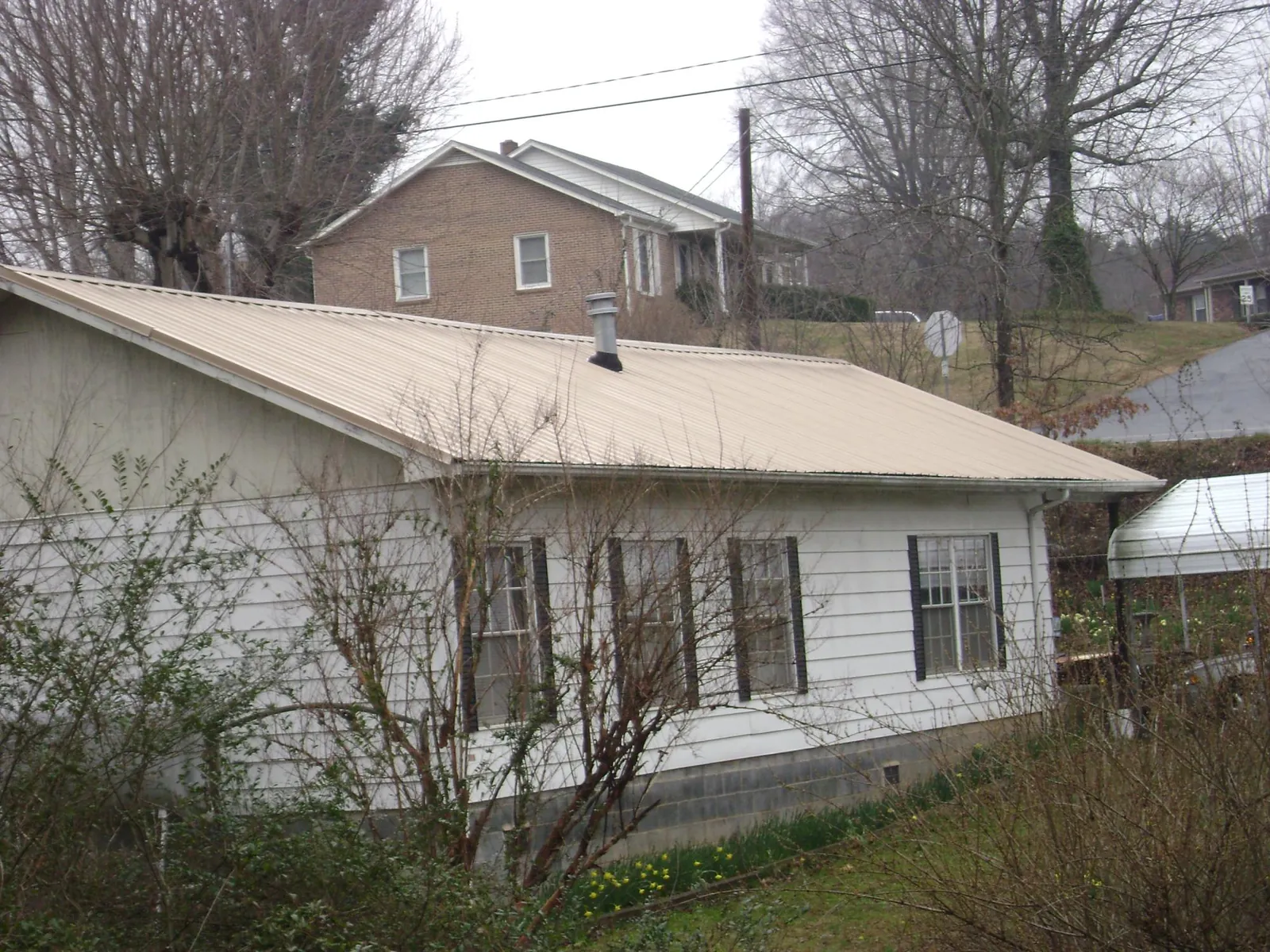 Tan metal roof on a white sided house set into a hillside — Commercial Roofing by Roofing Brothers in Bernard